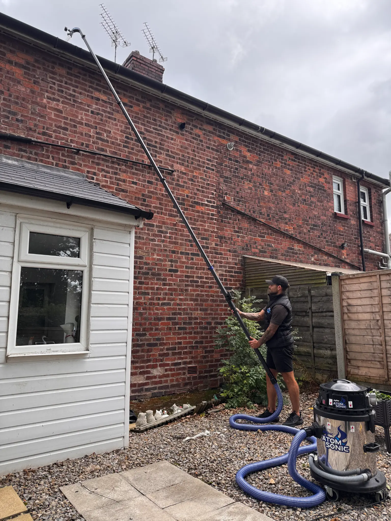 Exterior cleaning technician using a gutter-vacuum pole at a brick home